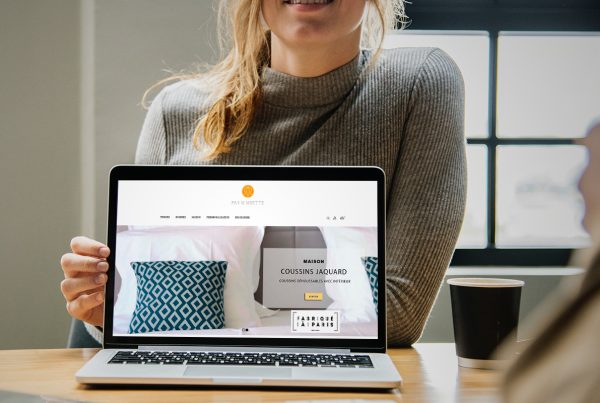 Imagen de mujer sujetando una laptop enseñando un sitio web de complementos de moda y de hogar