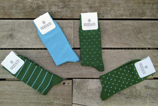 Foto de cuatro calcetines, tres de color verde y uno de color azul encima de un trozo de madera junto con su etiqueta de marca